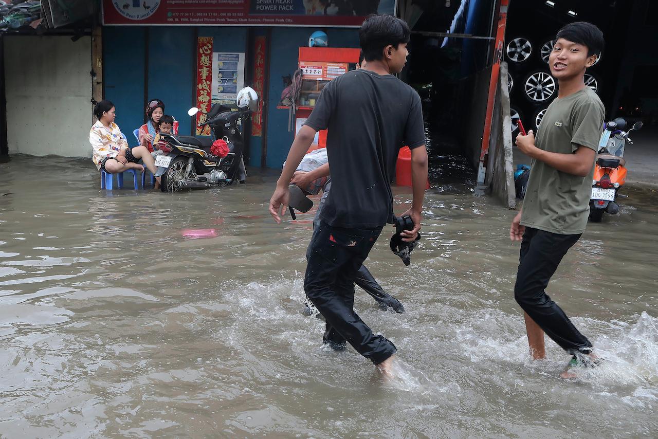 Teenagers wade through a flooded street following recent rains in Phnom Penh, Cambodia on Oct 12. Photo: AP