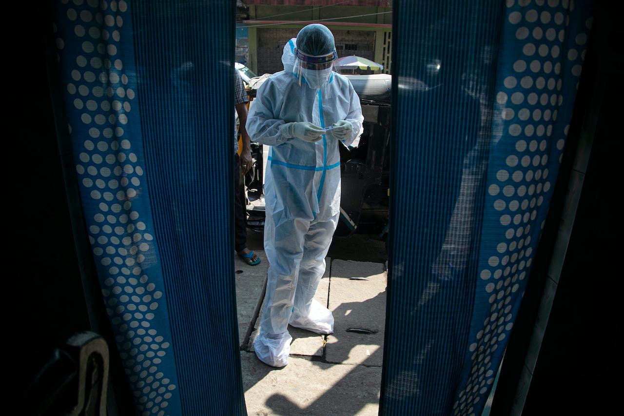 A health worker wears protective equipment as he takes random tests of people for Covid-19 in a market in Gauhati, India, Oct 16. Photo: AP