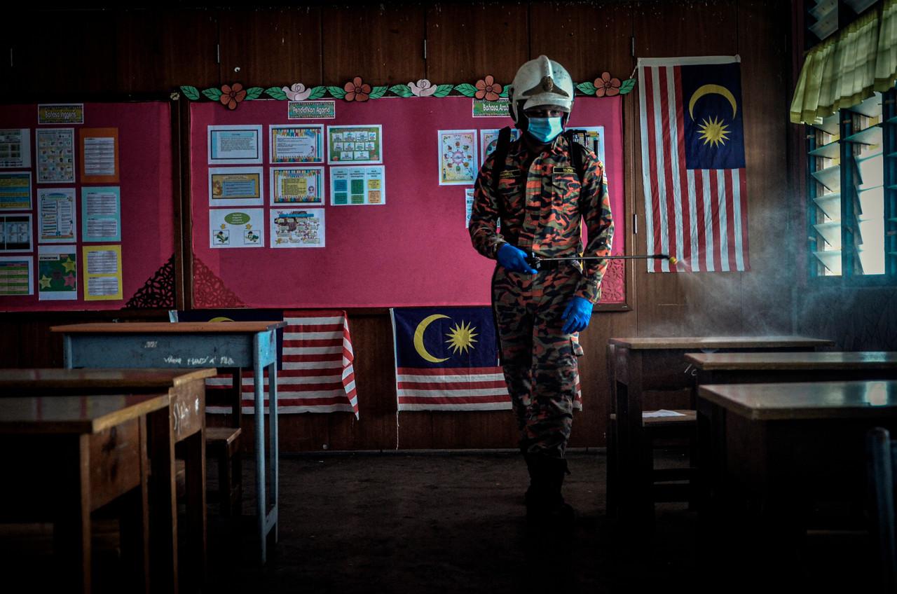 A fire and rescue worker sprays a classroom with sanitiser at a school in Perai. Photo: Bernama
