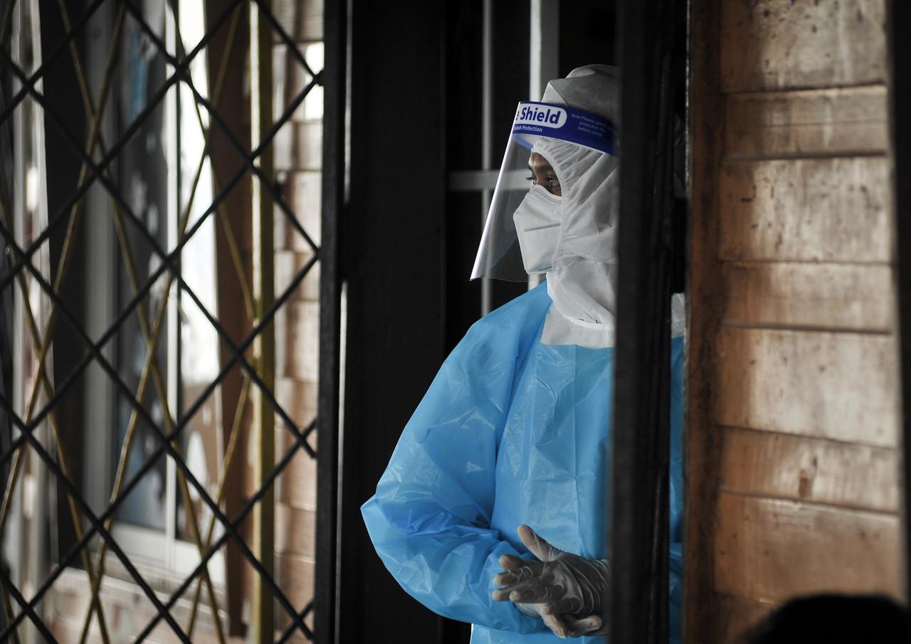 A health worker wearing personal protective equipment looks out of a house in a water village in Labuan where residents are being screened for Covid-19. Photo: Bernama