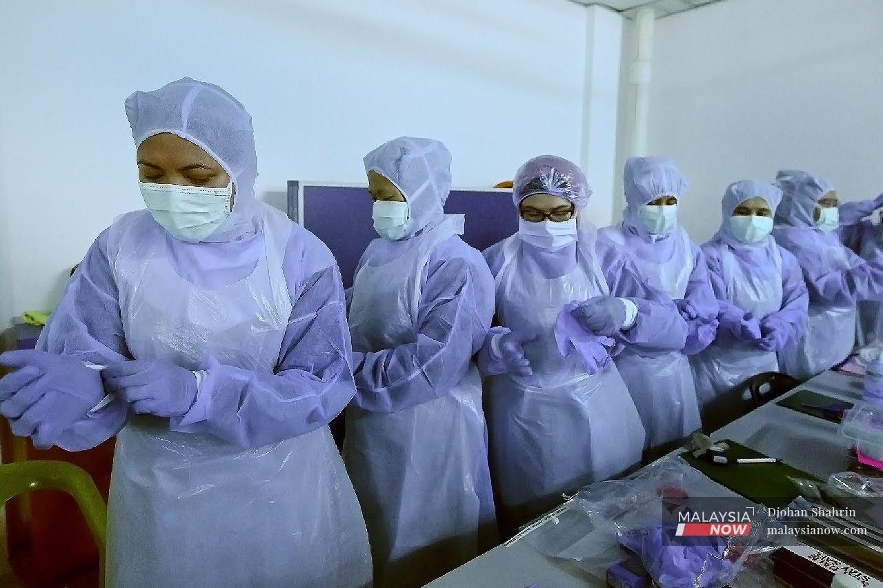 Para petugas kesihatan lengkap dengan sut PPE sebelum menjalankan ujian saringan Covid-19.
