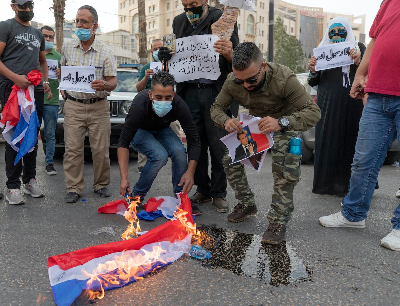 Palestinian protesters burn representations of French flags and pictures of French President Emmanuel Macron during a protest in the West Bank city of Ramallah on Oct 27. Photo: AP