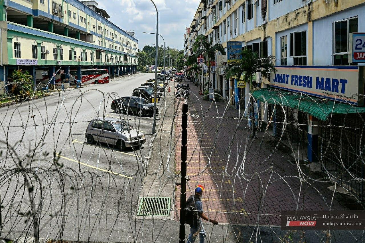 A resident walks past a barbed wire fence, put up at Plaza Hentian Kajang in Selangor following the government's announcement of an enhanced movement control order in the area until Nov 10.