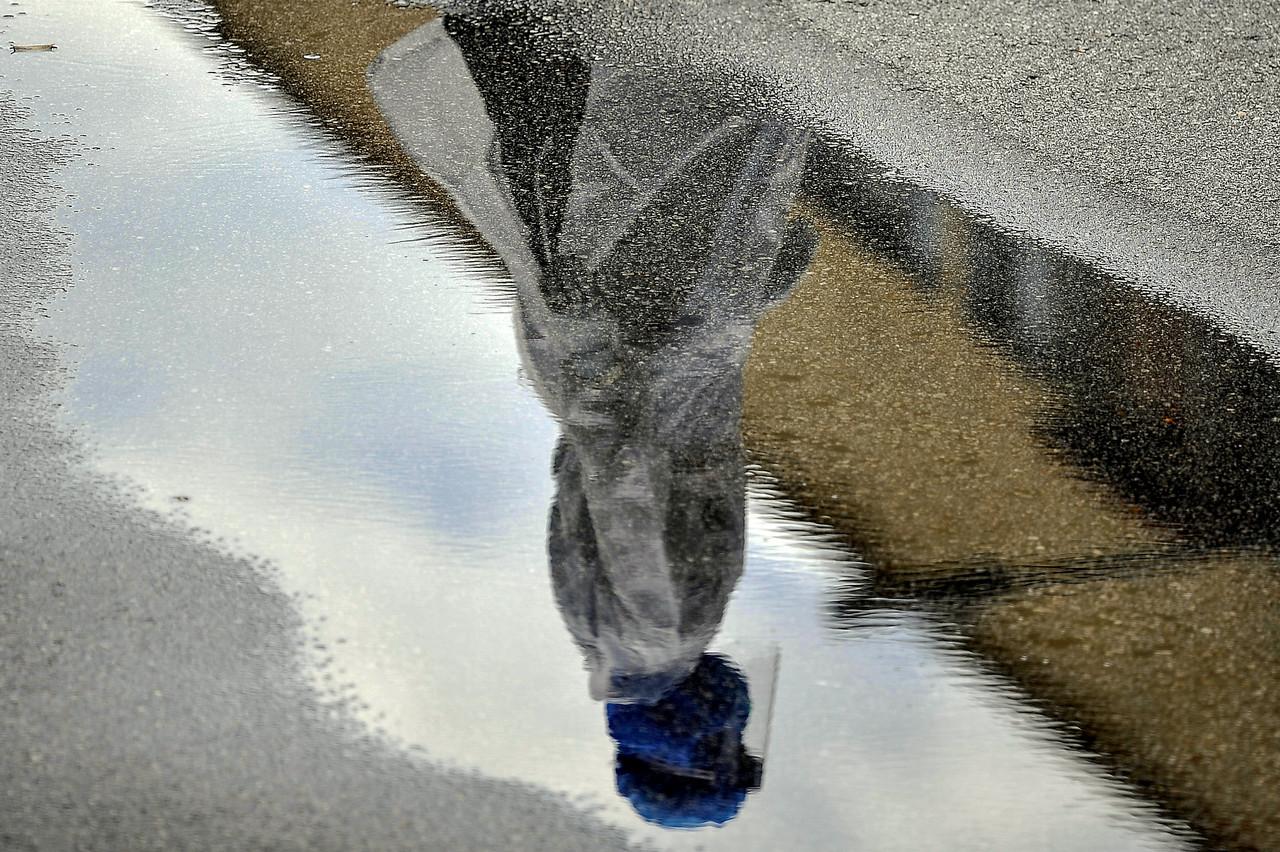 A member of the Civil Defence Force dressed in protective gear is reflected in a puddle as he monitors a Covid-19 screening at Plaza Hentian Kajang. Photo: Bernama