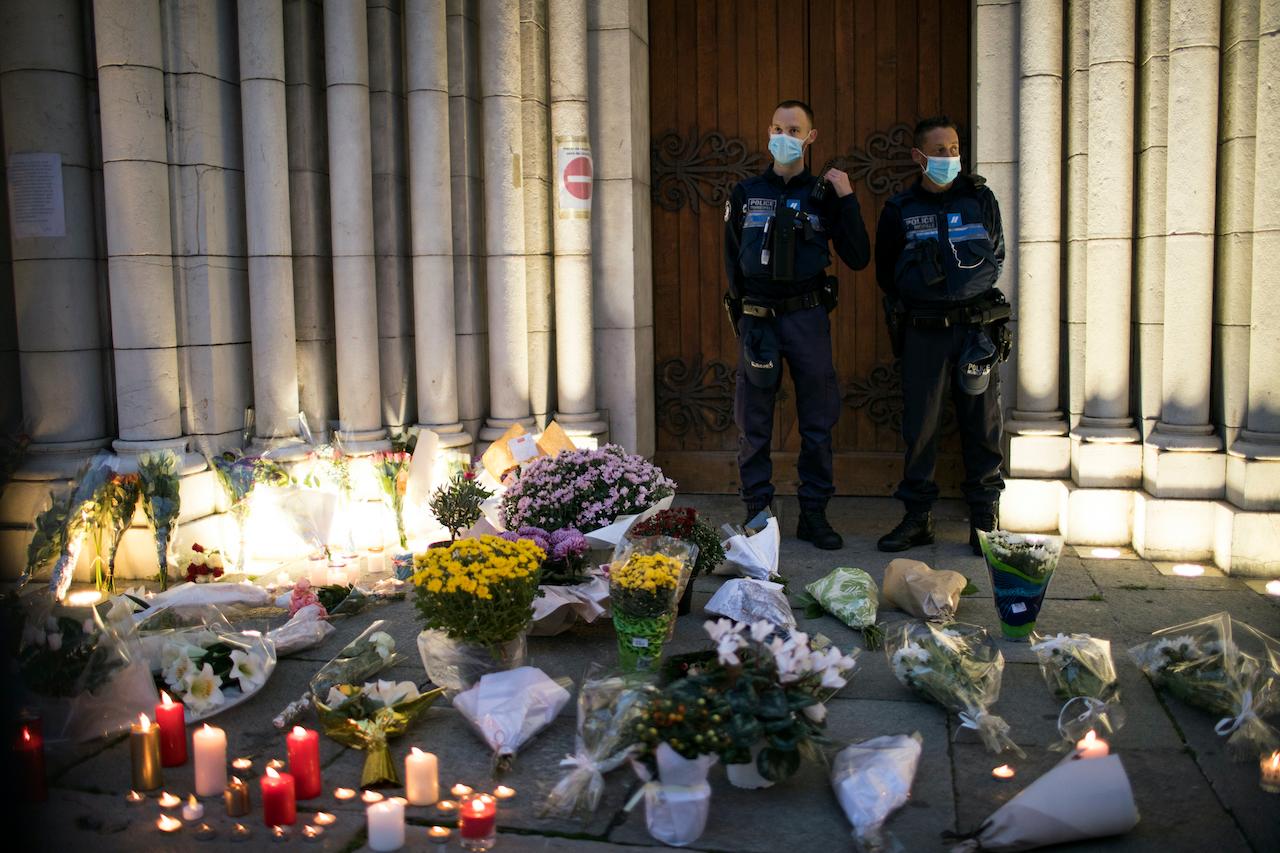 Police stand next to flowers and candles set on the steps of the Notre Dame church in Nice, France on Oct 30. Photo: AP