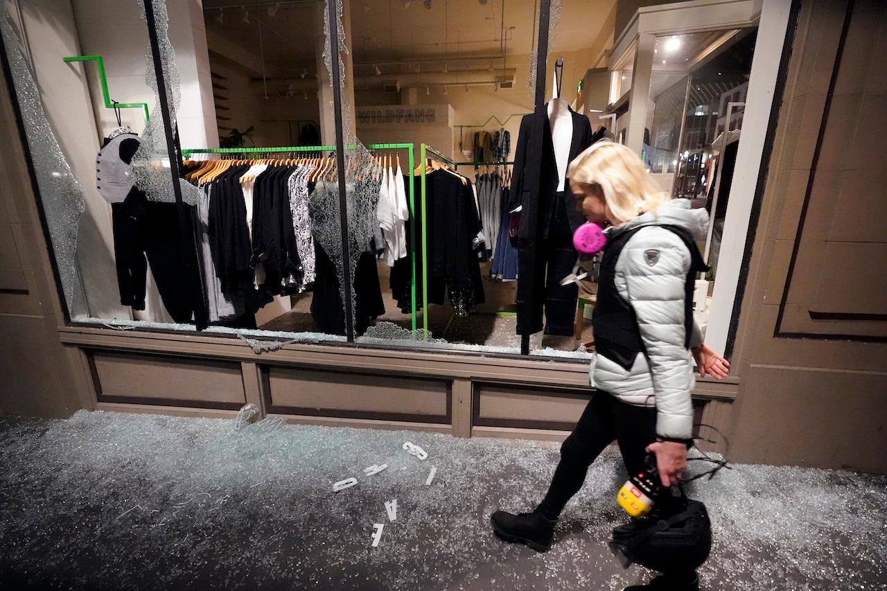 A woman walks over broken glass and past a shattered store window following protests on Nov 4 in Portland, Oregon. Photo: AP