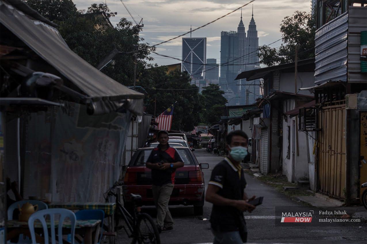 Pedestrians walk by a row of makeshift stalls in Kuala Lumpur with the Twin Towers in the background.