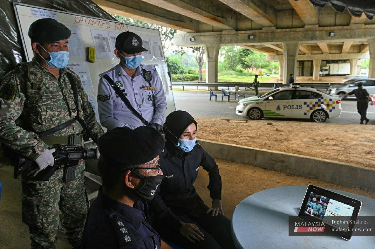 Petugas barisan hadapan mengikuti pembentangan Belanjawan 2021 pada Jumaat lepas, semasa waktu rehat ketika menjalankan sekatan jalan raya di Lebuh Sentosa di Putrajaya.