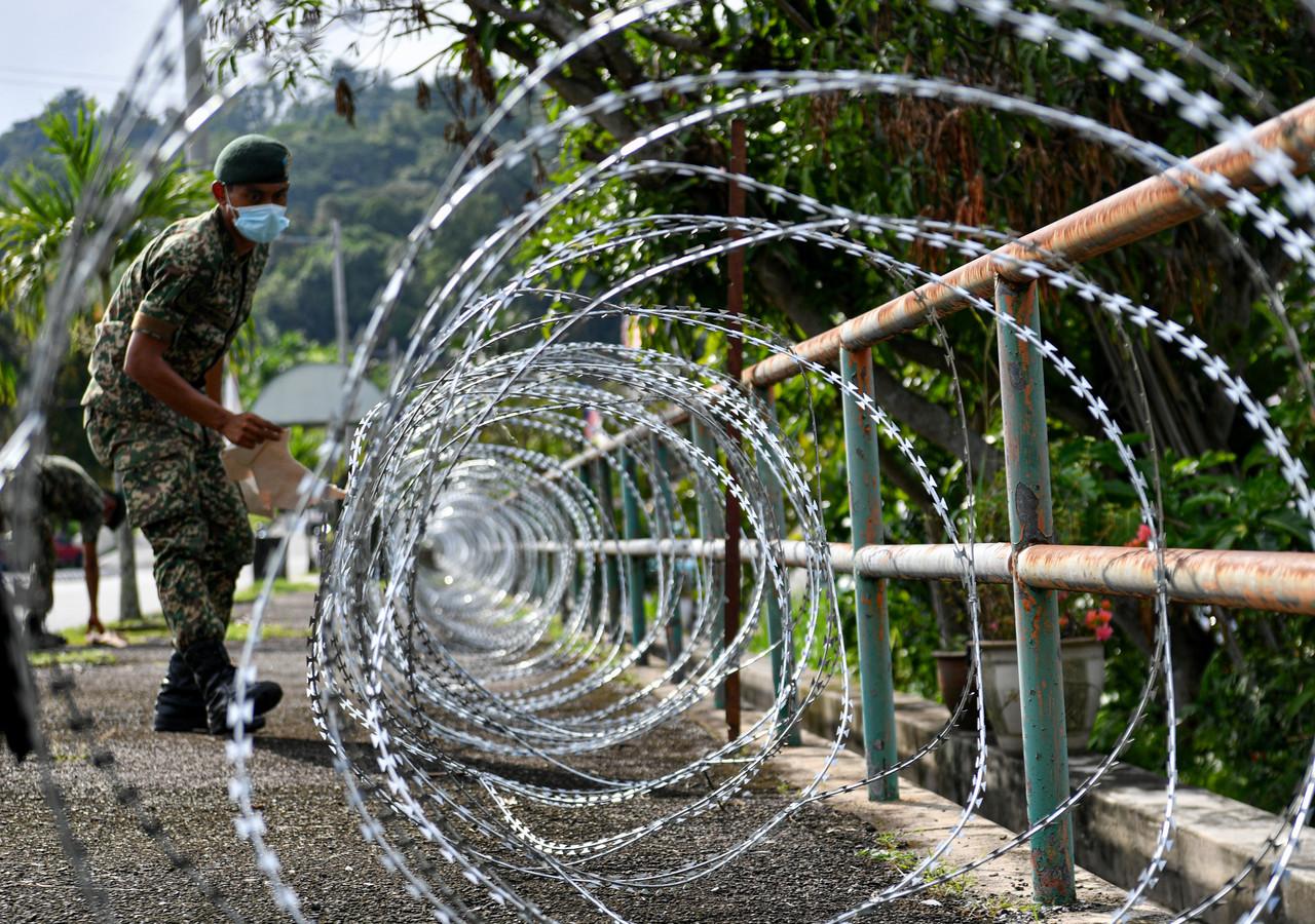 A member of the armed forces puts up a barbed wire fence at the Taman Meru 2 C area in Ipoh, which has been placed under a two-week enhanced movement control order. Photo: Bernama