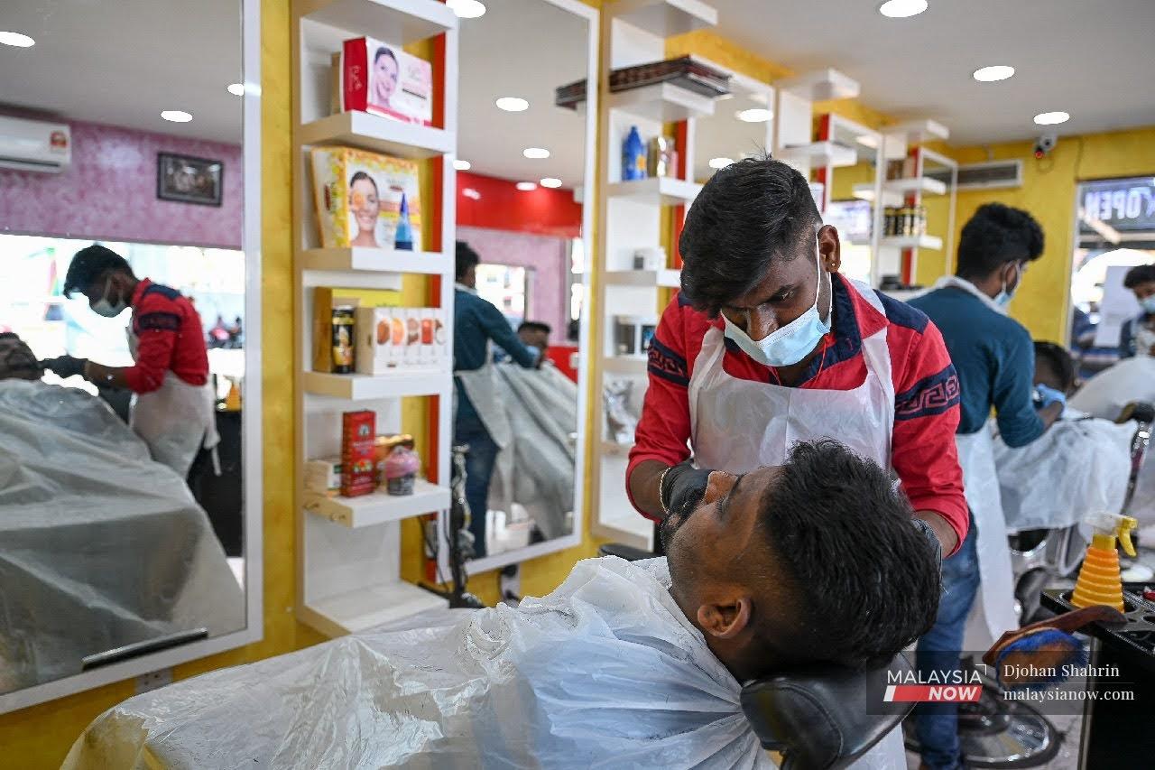 Seorang tukang gunting rambut di Brickfield, Kuala Lumpur mematuhi SOP yang ditetapkan kerajaan ketika mengunting rambut pelanggannya.
