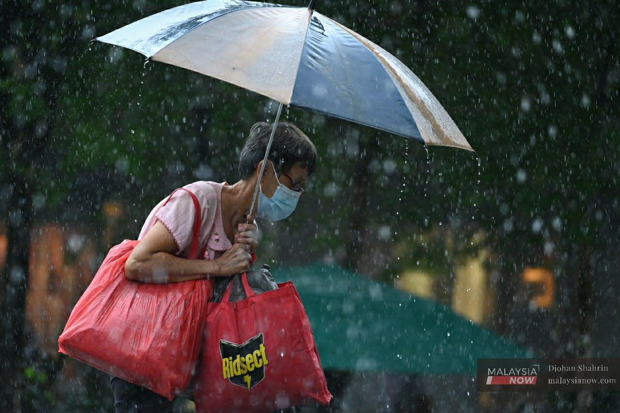 A senior citizen crosses the road in the rain at Jalan Dang Wangi in Kuala Lumpur.