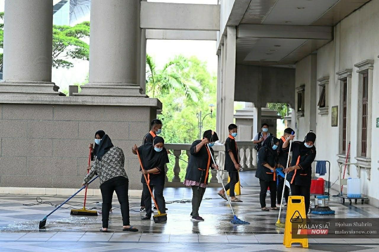 Sekumpulan pekerja pembersihan memakai pelitup muka ketika membersih ruang legar Kompleks Mahkamah Jalan Duta, Kuala Lumpur.
