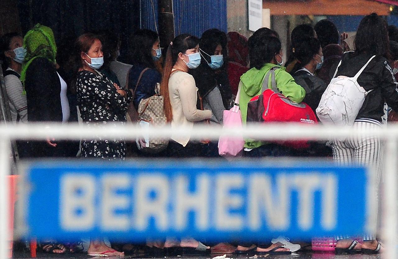 Top Glove workers wait in line to be escorted by health workers out of their hostel in Meru, Klang. Photo: Bernama