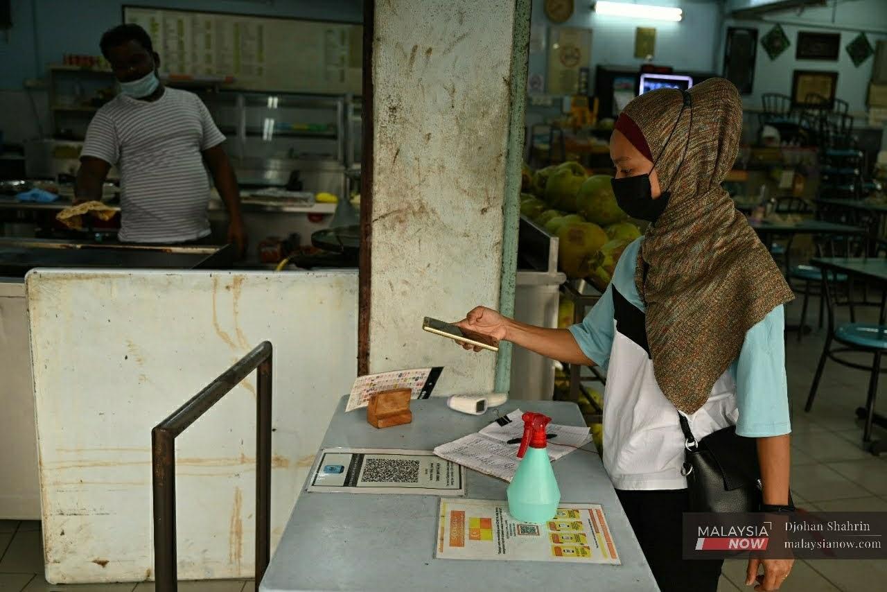 Seorang wanita menggunakan aplikasi MySejahtera ketika memasuki sebuah restoran di Taman Tasik Ampang, Kuala Lumpur.