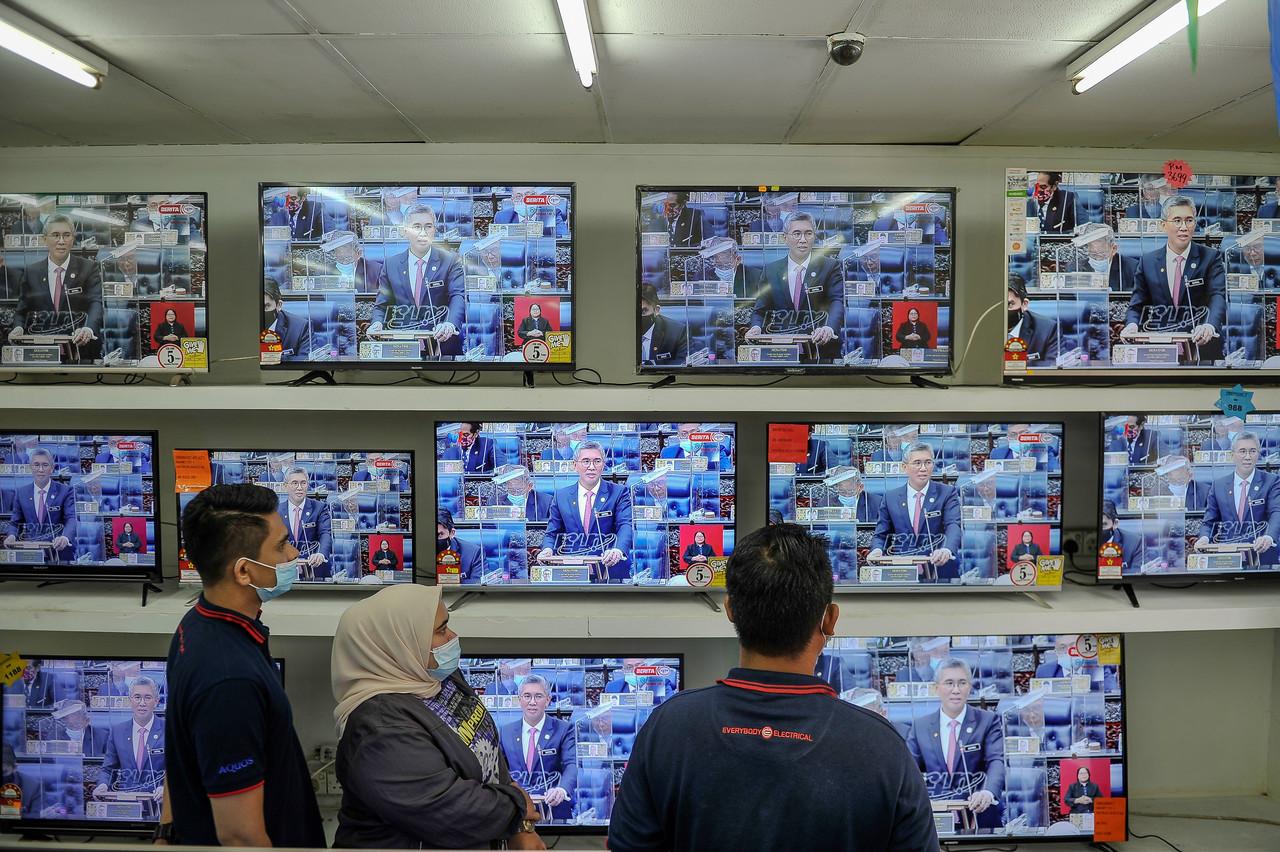 Customers in an electronics shop watch as Finance Minister Tengku Zafrul Aziz gives the winding-up speech on the 2021 budget in the Dewan Rakyat yesterday. Photo: Bernama