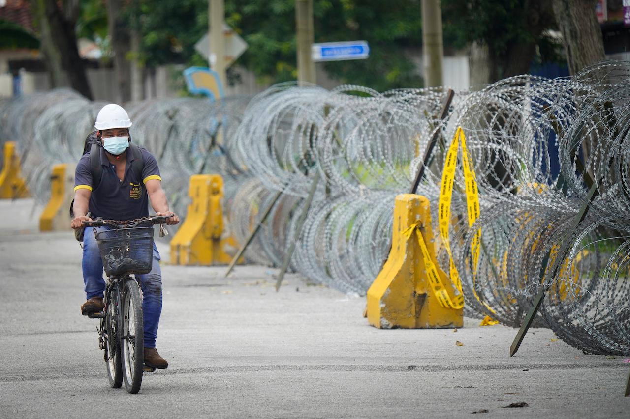 A man cycles next to coils of barbed wire near the Top Glove factory hostel in Shah Alam, Nov 25. Photo: AP