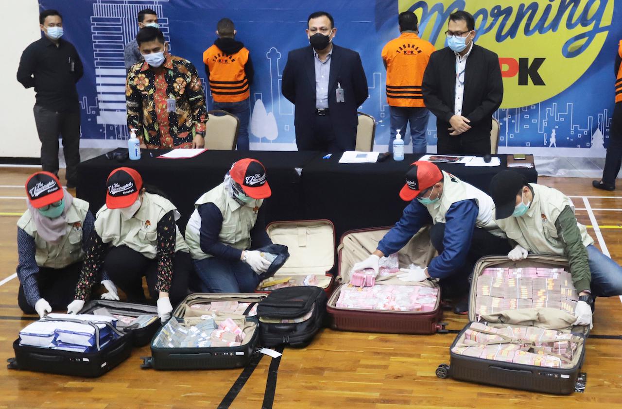 Officers arrange suitcases full of rupiah and US dollar bills confiscated from suspects as chairman of Indonesia's Corruption Eradication Commission Firli Bahuri (top centre) looks on during a news conference on a corruption case involving government's Covid-19 pandemic aid distribution, in Jakarta, Indonesia, Dec 6. Photo: AP