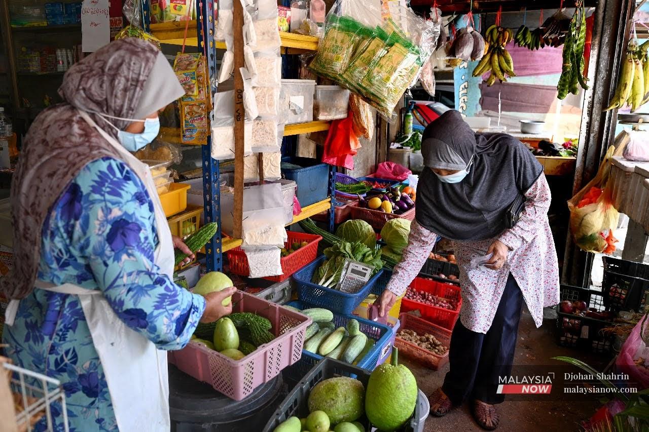 Seorang pelanggan memakai pelitup muka ketika membeli barang keperluan harian di sebuah kedai runcit di kampung Pandan, Kuala Lumpur.