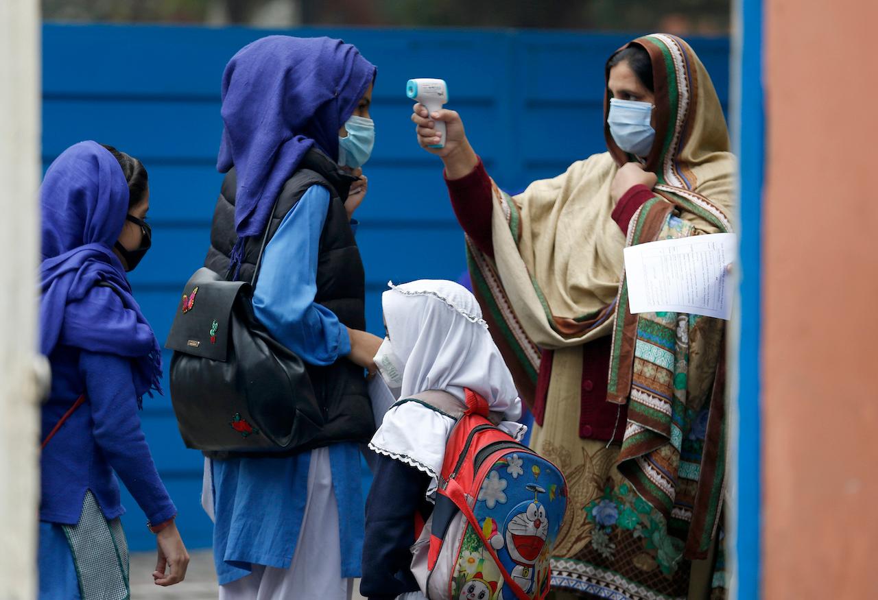 A teacher checks the temperatures of students as they arrive at a school in Lahore, Pakistan, Nov 25. Photo: AP