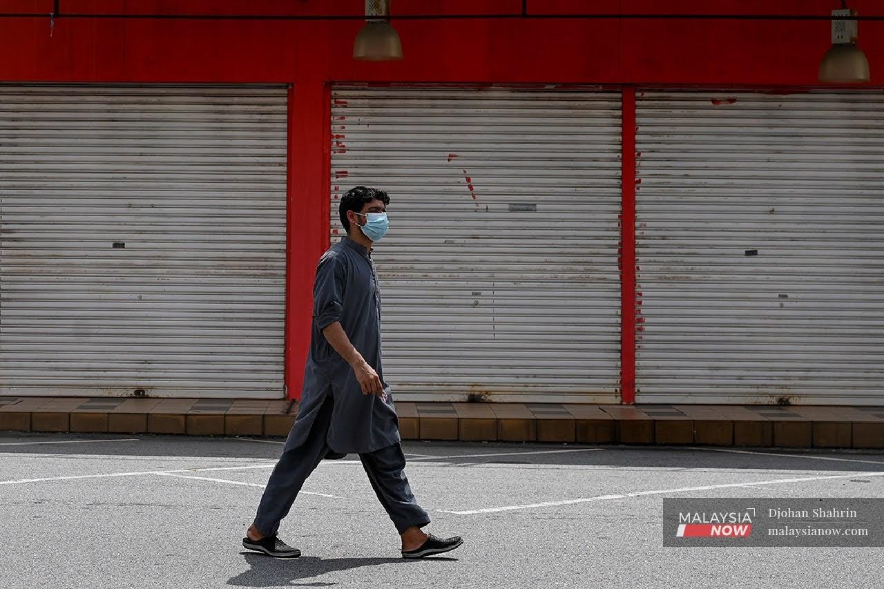 Seorang lelaki warga asing dilihat memakai pelitup muka ketika melalui deretan kedai di kawasan Nilai 3, Negeri Sembilan. Difahamkan banyak kedai-kedai di kawasan itu ditutup selepas terjejas akibat Covid-19.