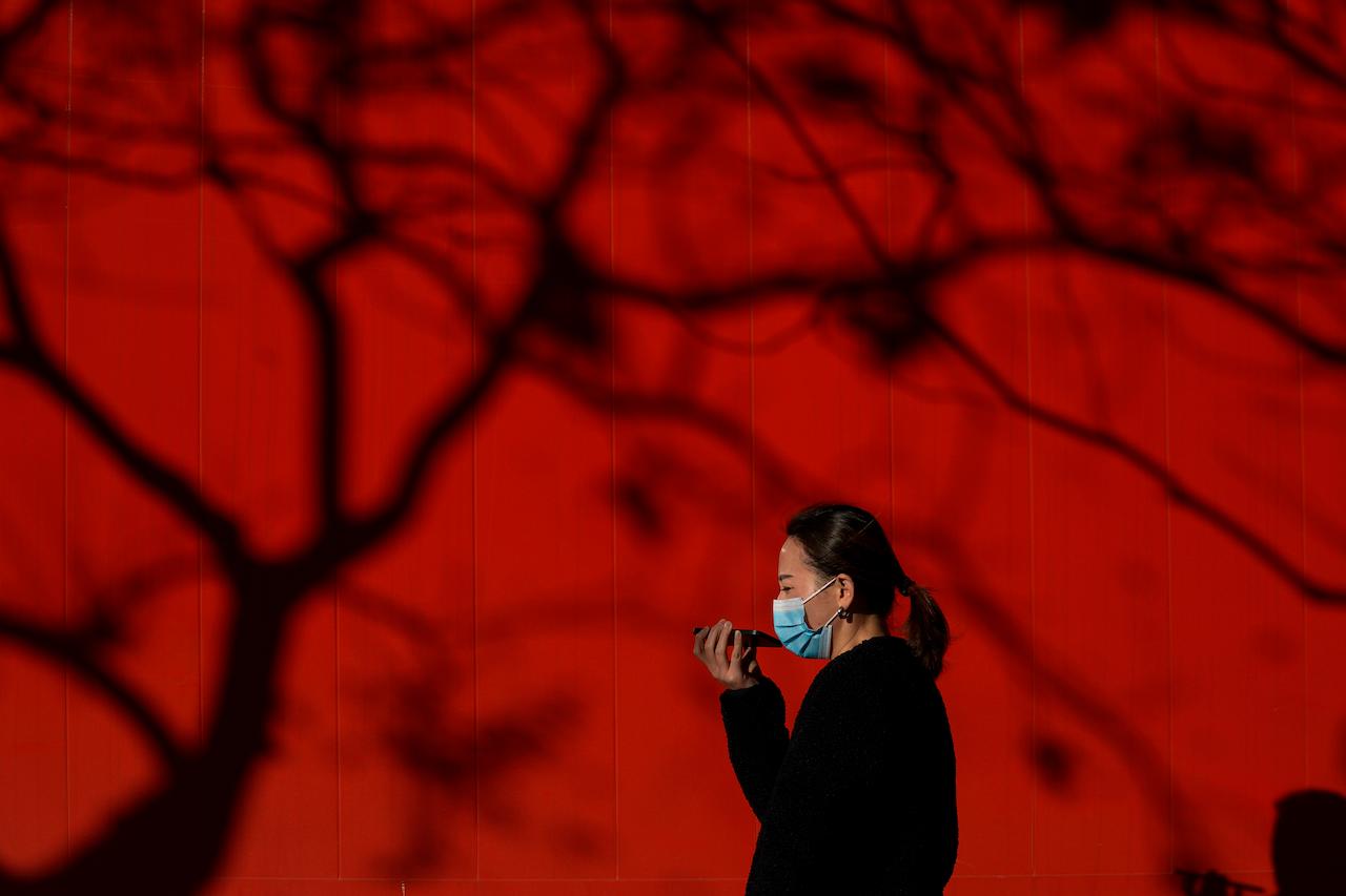 A woman wearing a face mask to help curb the spread of the coronavirus talks on her smartphone as she walks on a street in Beijing, Dec 7. Photo: AP