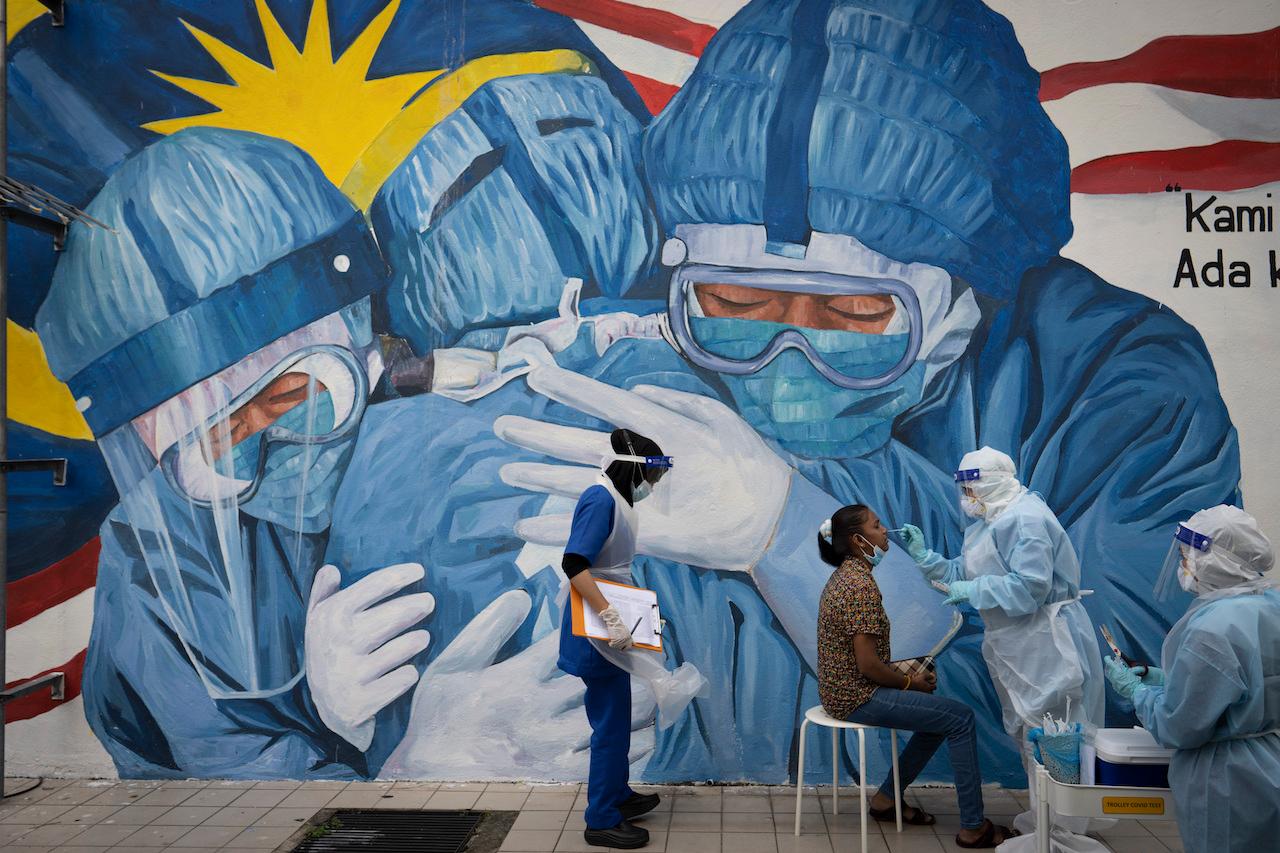 A doctor collects a sample for testing at a Covid-19 screening facility near a mural depicting medical frontliners in Shah Alam, Selangor on Dec 12. Photo: AP