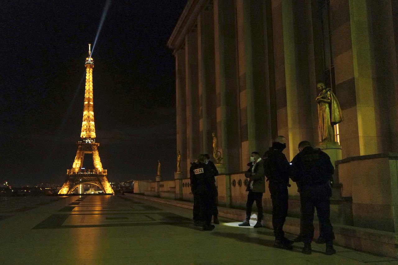 French police officers stop a person near the Eiffel Tower as they enforce a new curfew in Paris, Dec 15. Photo: AP