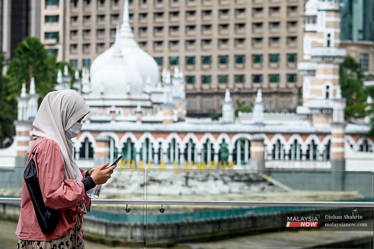 A woman looks at her phone as she walks through the Masjid Jamek area in downtown Kuala Lumpur.