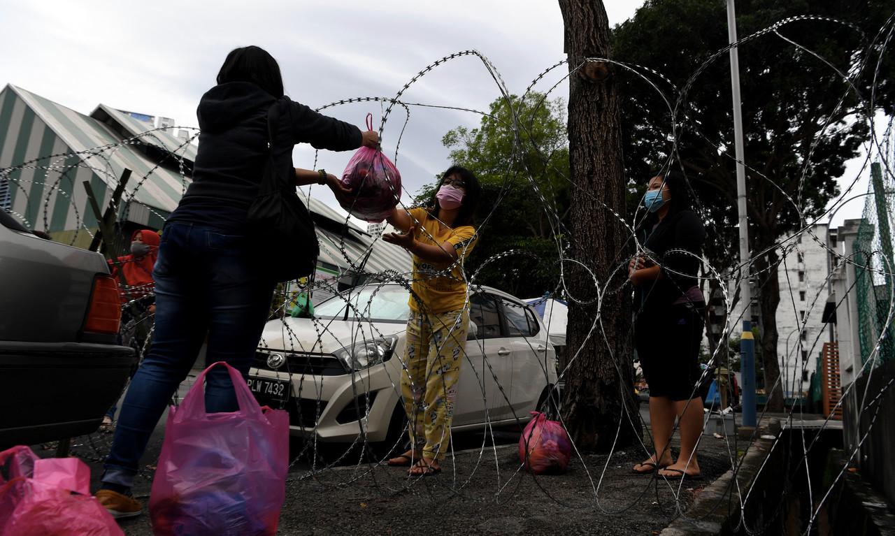 A woman hands a bag of daily necessities to a friend through a barbed wire fence at the Persiaran Paya Terubong Relau flats in George Town, where the enhanced movement control order has been extended until Dec 31. Photo: Bernama