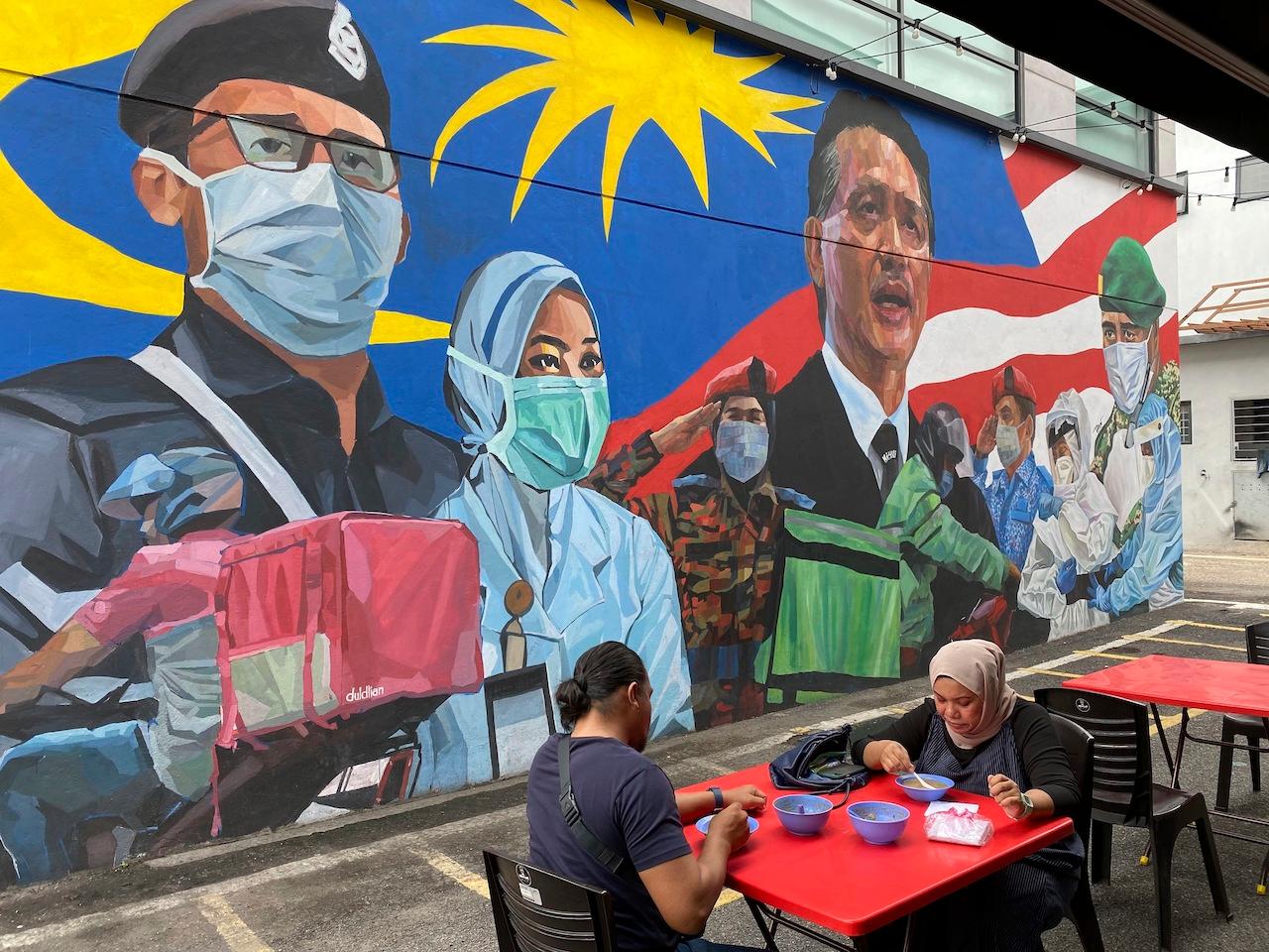 A couple have lunch next to a graffiti tribute to frontline workers at Damansara, Selangor. Photo: AP
