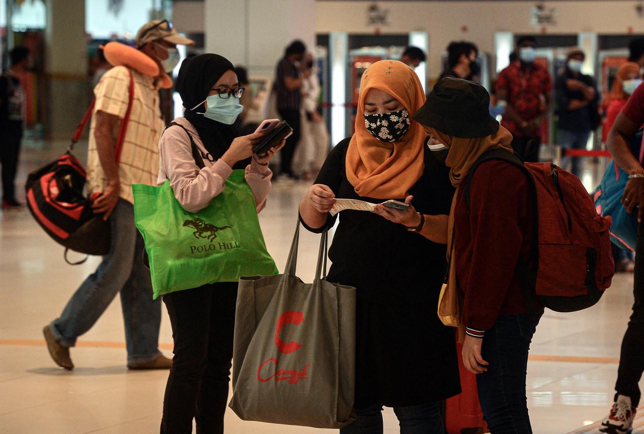 Travellers heading back to their hometowns for the holidays check their phones at the Southern Integrated Terminal in Kuala Lumpur. Photo: Bernama