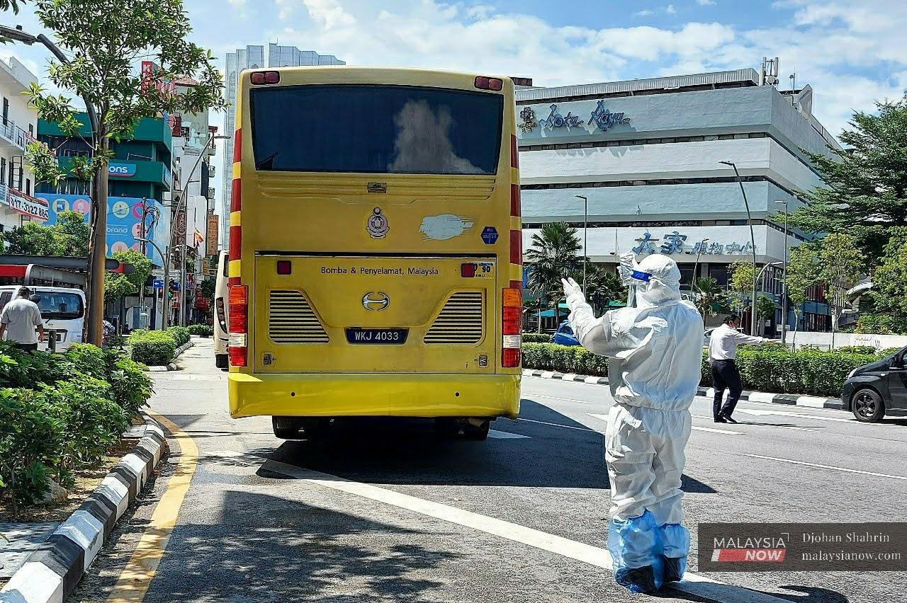 A frontline worker wearing protective gear gestures to a bus carrying people from the Menara Wang cluster in Kuala Lumpur to a hotel for the mandatory 14-day quarantine.
