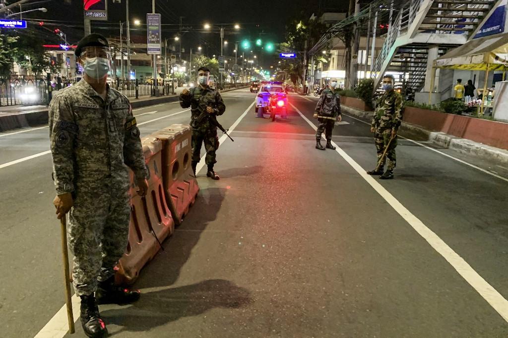 Policemen wearing face masks and shields as a preventive measure against the Covid-19 virus stand guard at a checkpoint in an almost empty road in Manila, Dec 24. Photo: AFP