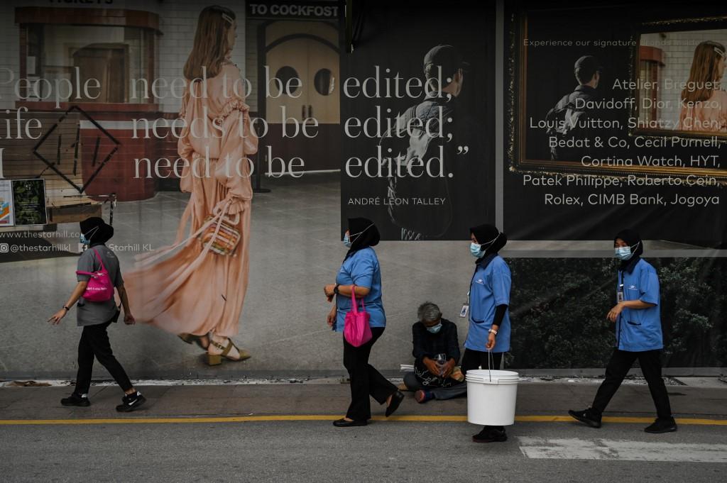 Women wearing face masks walk past a homeless man in Kuala Lumpur. Photo: AFP