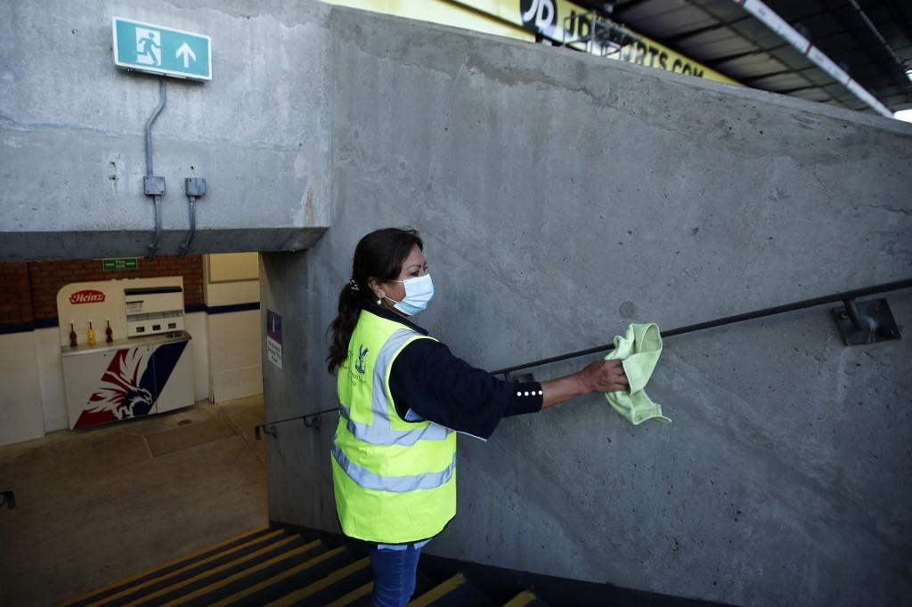 A member of staff cleans a hand rail ahead of an English Premier League football match between Crystal Palace and Manchester United at Selhurst Park in south London, July 16. The Premier League says it has confidence in its Covid-19 protocols and will not pause the season despite a string of virus cases. Photo: AFP