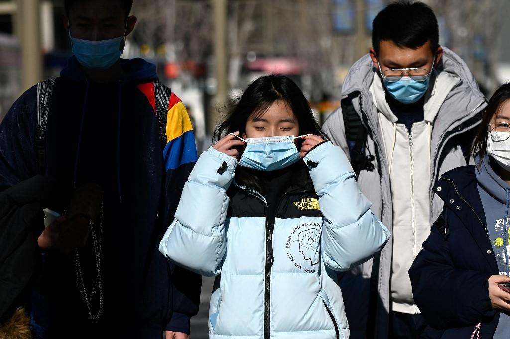 People wearing face masks walk along a street in Beijing, Dec 31. Photo: AFP