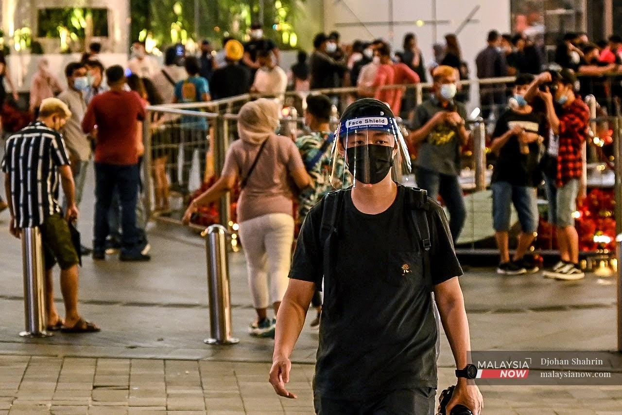 Seorang pejalan kaki dilihat memakai pelindung dan pelitup muka ketika bersiar-siar di sekitar Bukit Bintang, Kuala Lumpur pada malam menjelang tahun baru 2021.