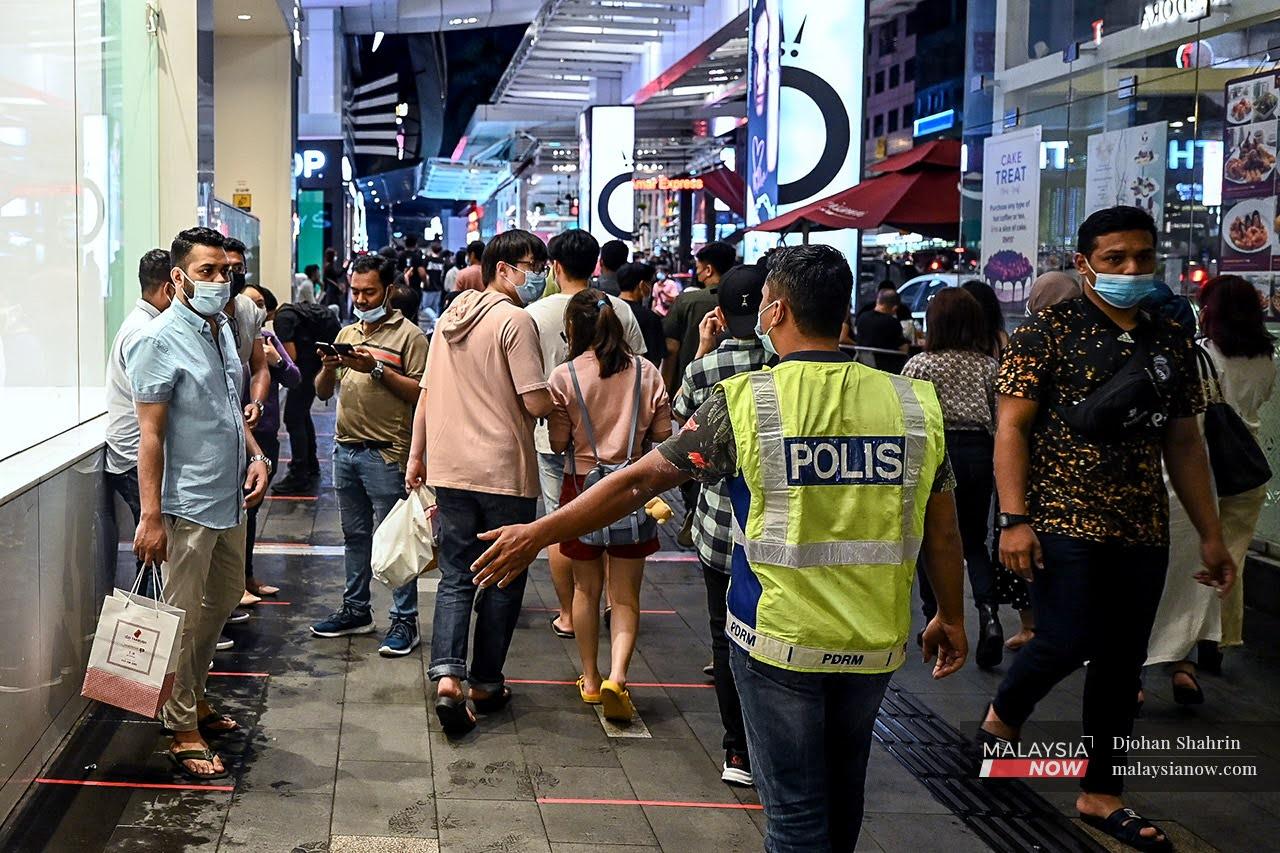 A police officer monitors the crowd to ensure adherence to health SOPs in the Bukit Bintang area in Kuala Lumpur.