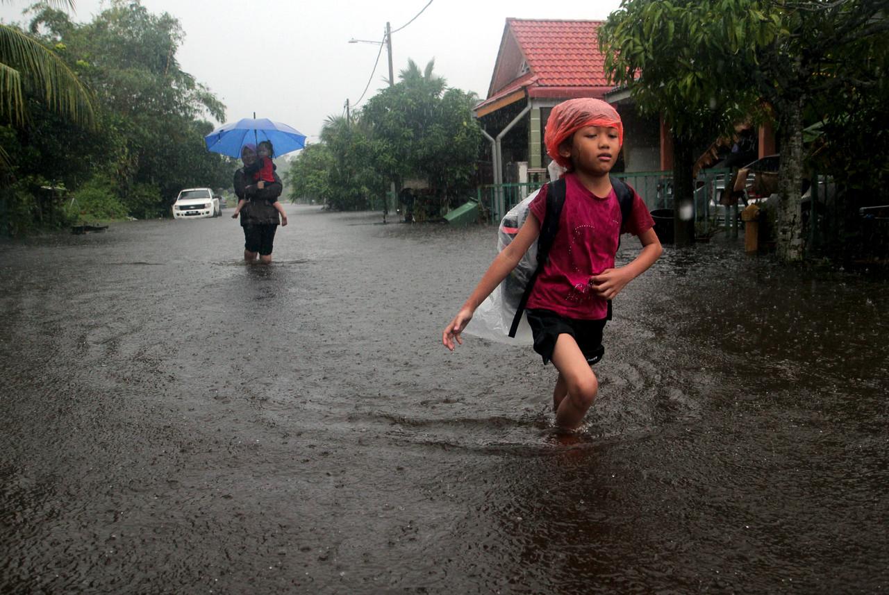 Seorang ibu bersama dua anaknya meredah banjir yang melimpahi kawasan Taman Perumahan Kempadang Makmur, Kuantan semalam. Gambar: Bernama
