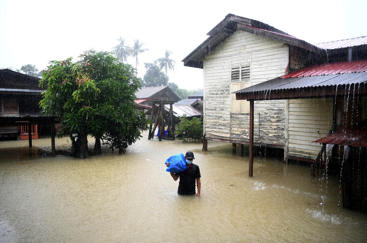 A villager in Kuantan, Pahang, carries his belongings on his shoulder while wading through flood waters one meter deep on Jan 3. Photo: Bernama
