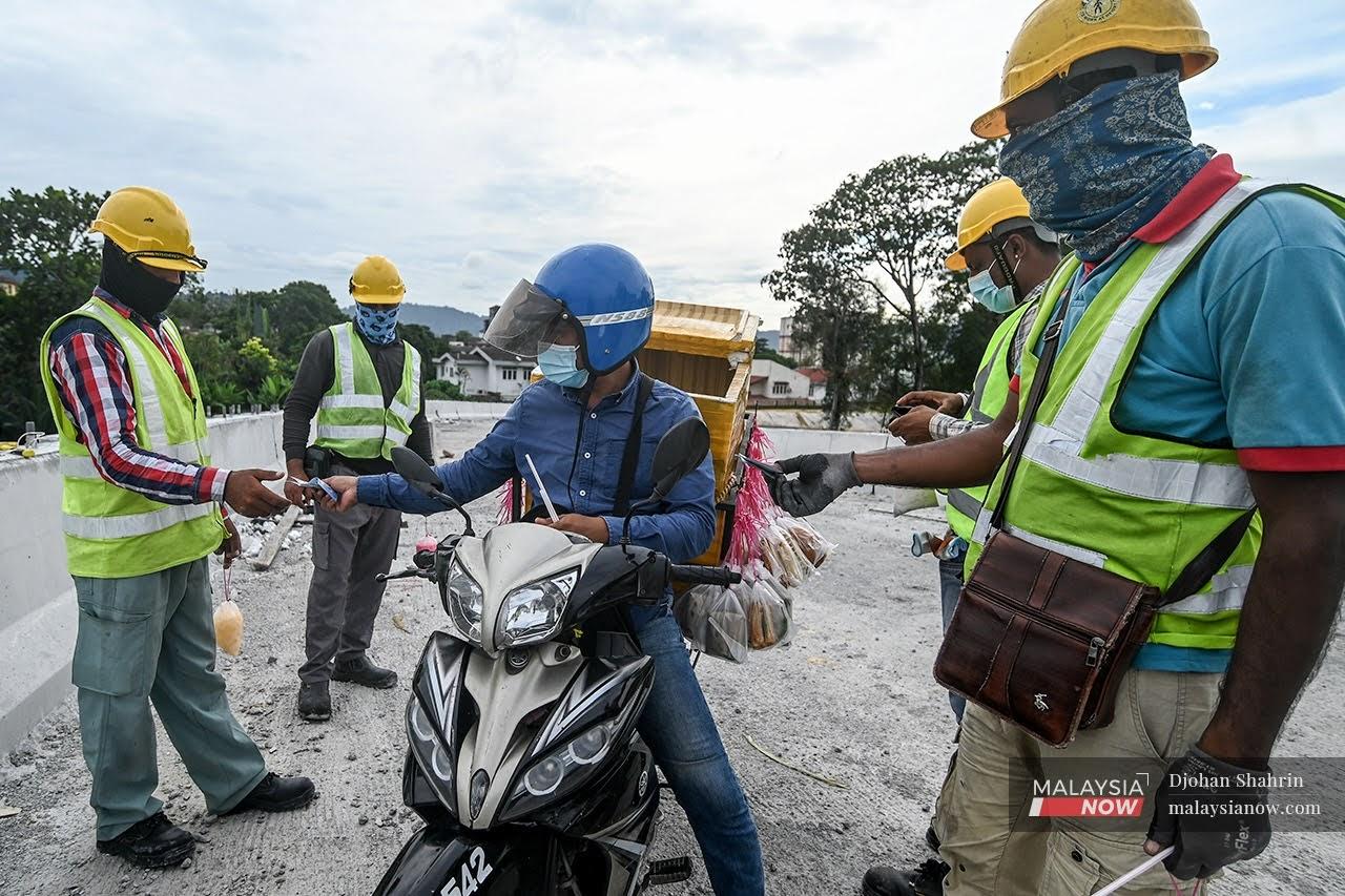 Pekerja sebuah tapak binaan warga asing memakai pelitup muka ketika membeli makanan yang dijual seorang penjaja bermotosikal di Kuala Lumpur.