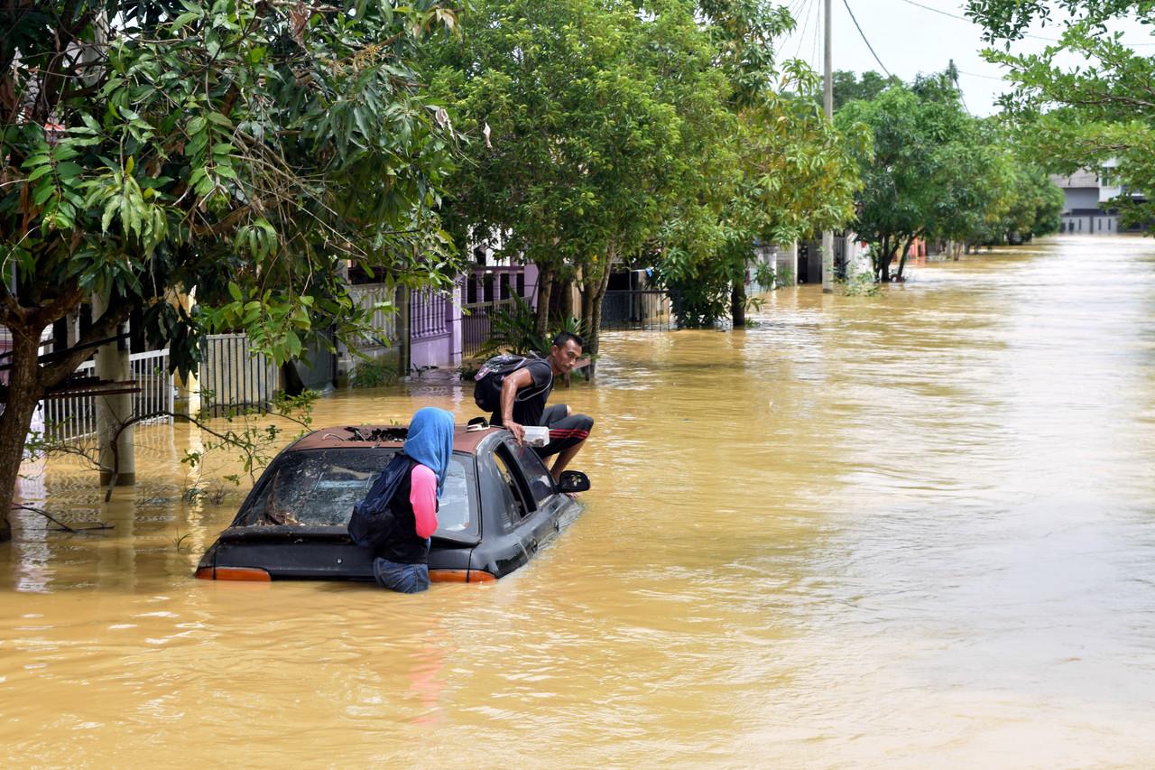 Kelihatan seorang lelaki berhenti seketika di atas sebuah kereta tersadai selepas meredah air di kawasan rumahnya di Kampung Baru Bukit Mentok, Kemaman yang ditenggelami air sejak Rabu lalu. Gambar: Bernama