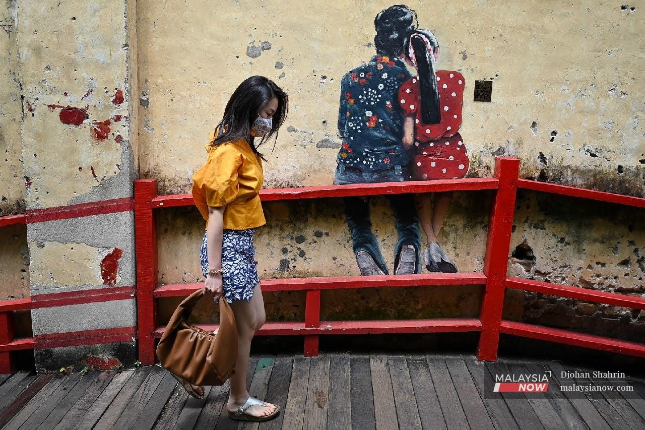 Seorang pejalan kaki memakai pelitup muka melalui kawasan lukisan mural Jalan Panggung, Kuala Lumpur.