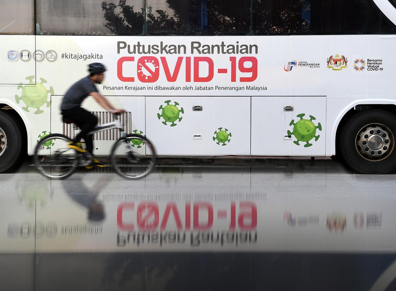 A cyclist cycles past a bus bearing a message urging people to work together to break the chain of Covid-19 infections in the country. Photo: Bernama