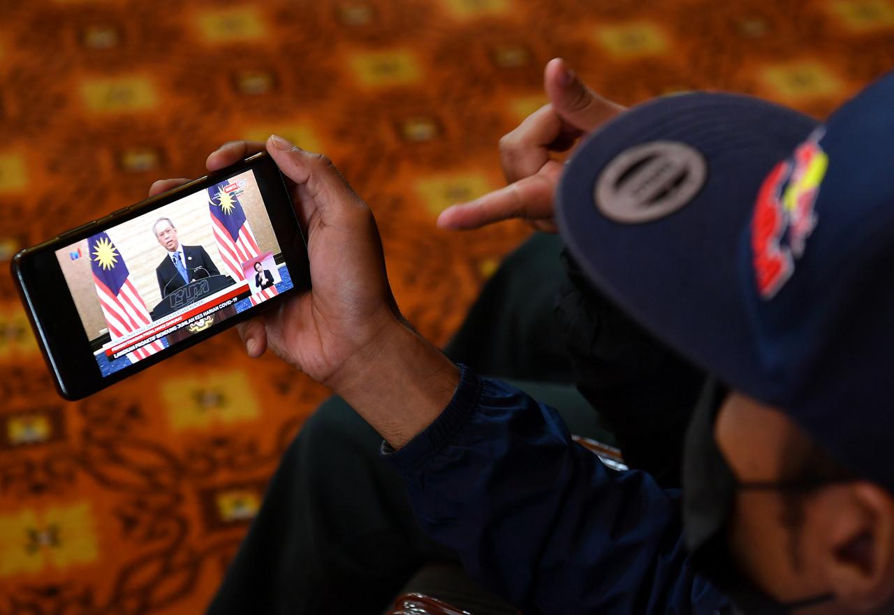 Orang awam mendengar pengumuman khas darurat oleh Perdana Menteri Muhyiddin Yassin hari ini melalui peranti digital. Gambar: Bernama