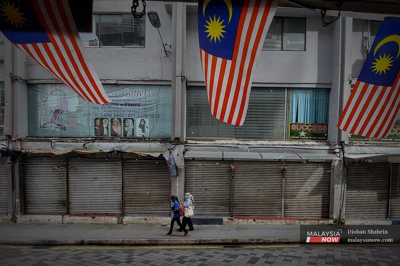 Pedestrians walk past a row of shops in Kuala Lumpur which have shuttered due to the movement control order which came into effect today.