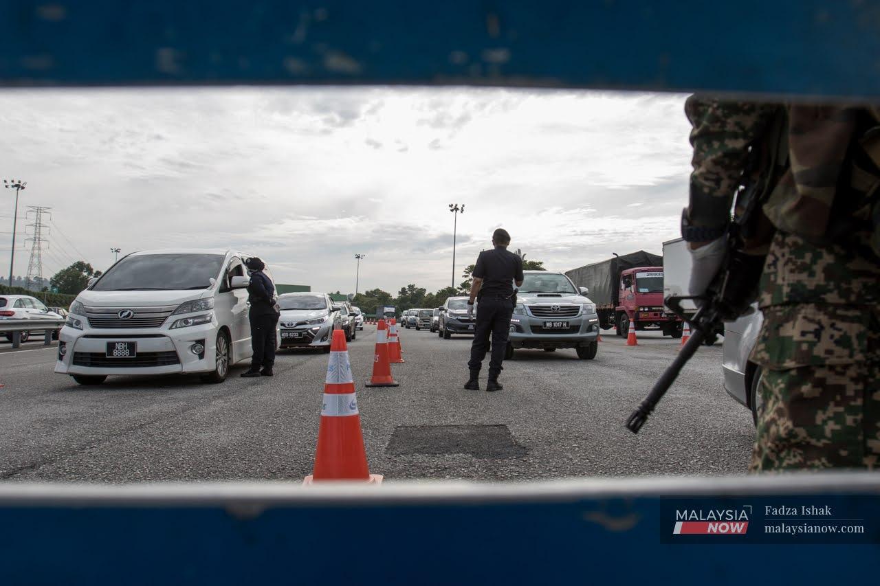 A member of the armed forces stands by the side as police officers check vehicles at a roadblock in Setia Alam, Shah Alam during the first movement control order period last year.
