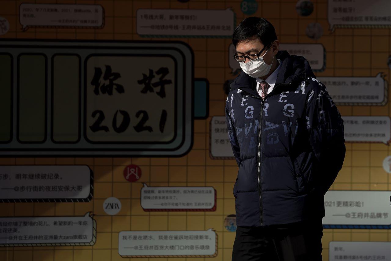 A man wearing a face mask to help curb the spread of the coronavirus walks by a greeting board at the Wangfujing shopping district in Beijing, Jan 18. Photo: AP