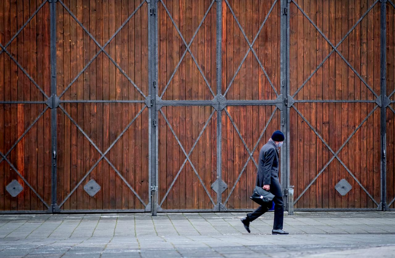 A man wearing a face mask walks past the gate of a former factory in Frankfurt, Germany, Jan 19. Photo: AP