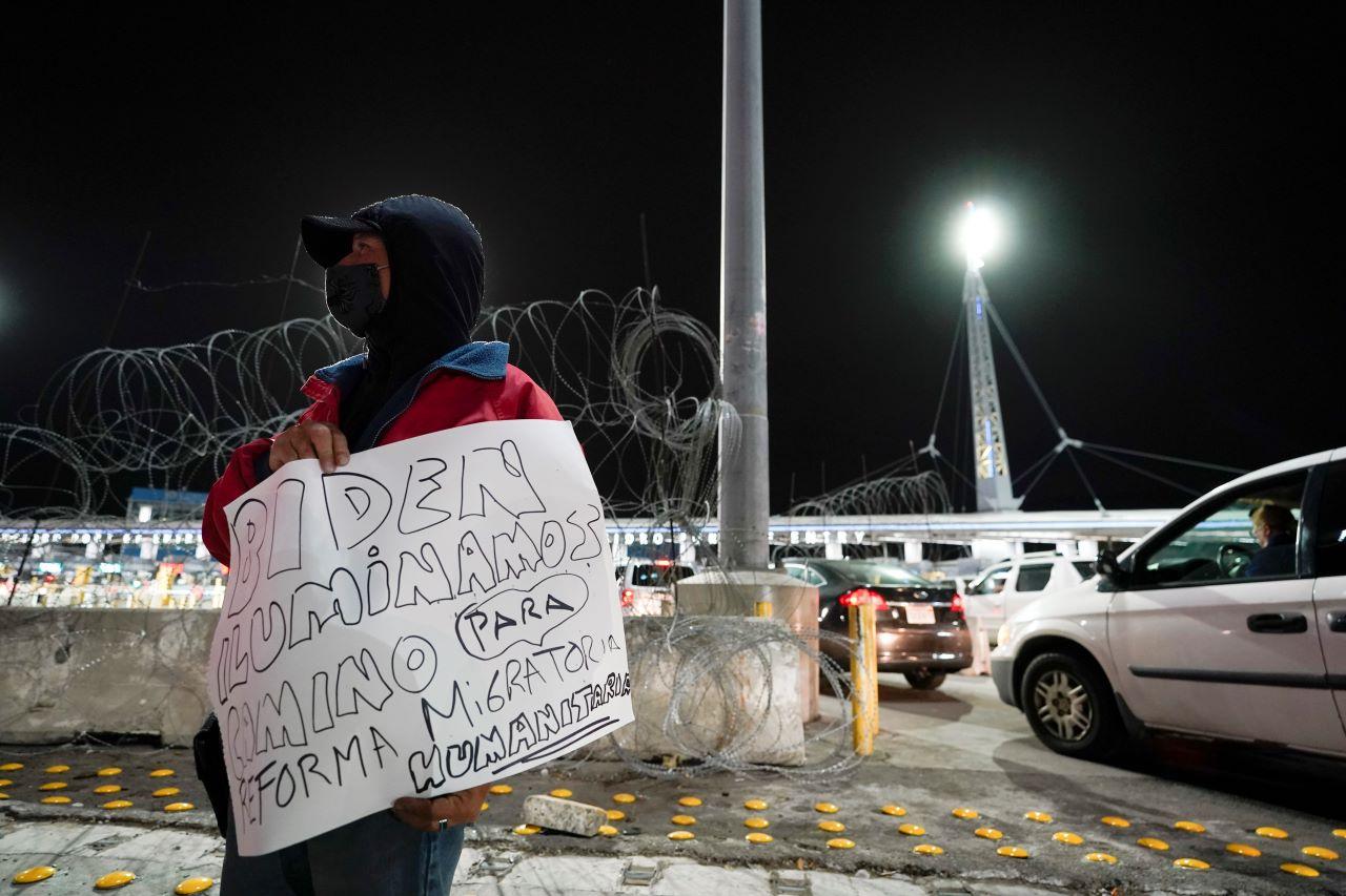 A man holds a sign during a vigil in support of migrants as he stands at the entrance to the San Ysidro Port of Entry along the border between the US and Mexico, Jan 19, in Tijuana, Mexico. Photo: AP